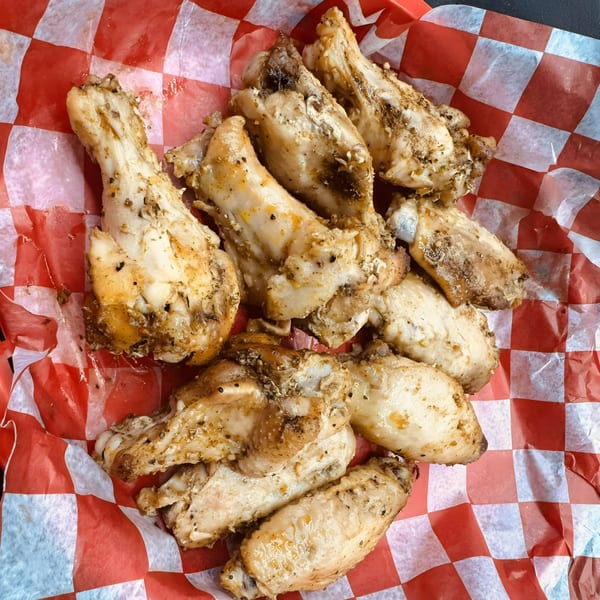 A pile of Smokin’ Jim's House of Bar-B-Q chicken wings on red and white checkered paper.