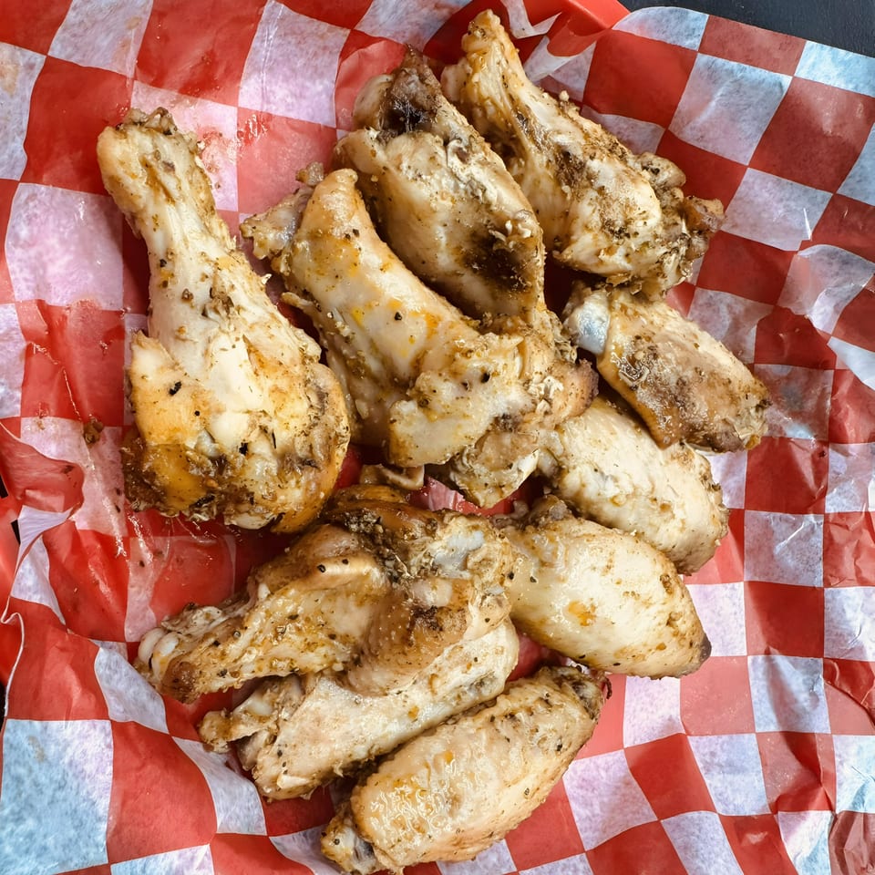 A pile of Smokin’ Jim's House of Bar-B-Q chicken wings on red and white checkered paper.