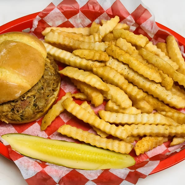 Smokin’ Jim's pulled pork sandwich, crinkle-cut fries, and a pickle spear in a red basket.