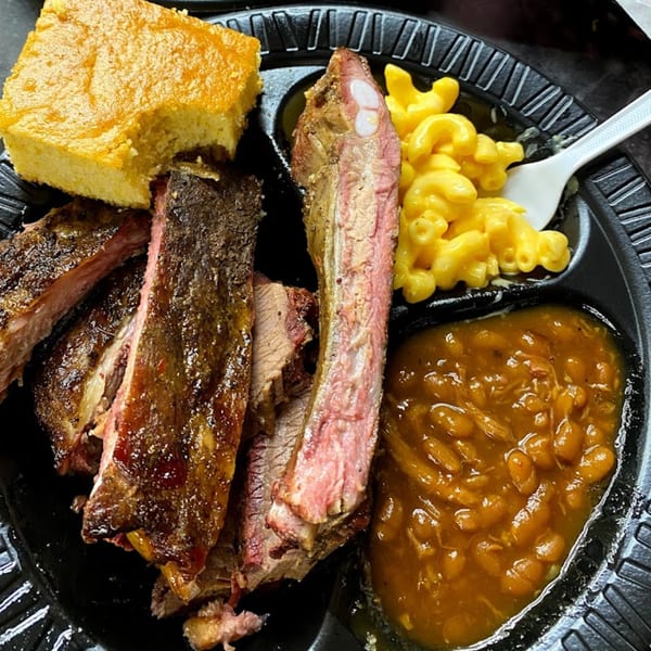 Smokin’ Jim's House of Bar-B-Q ribs, cornbread, mac and cheese, and baked beans on a black plate.