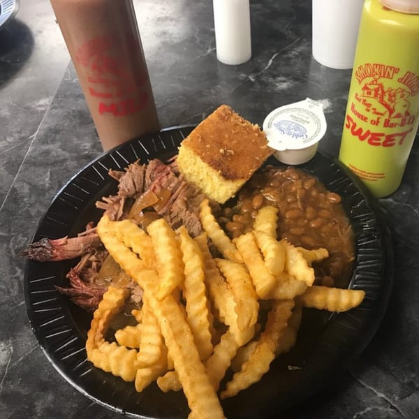 A Smokin' Jim's House of Bar-B-Q plate with brisket, crinkle fries, baked beans, and cornbread.