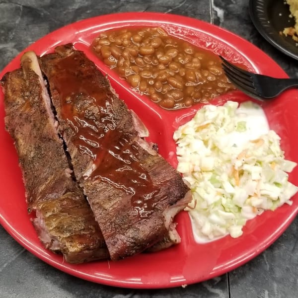 Smokin’ Jim's House of Bar-B-Q ribs with sauce, baked beans, and coleslaw on a red plate.